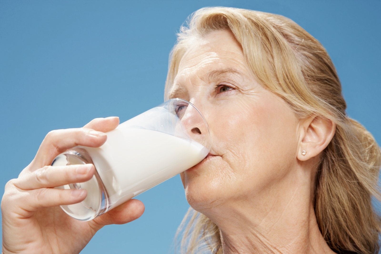 Closeup portrait of a healthy retired woman drinking glass of milk against clear sky