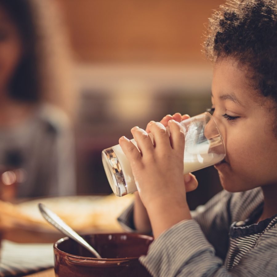 Small black boy drinking fresh milk during breakfast.